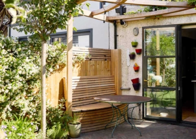 Back garden design in Frankfurt Road, 5 Patio, storage bench and table, beneath a pergola with wisteria.